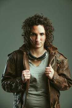 Frontal portrait of a female biker in leather jacket and goggles. She has a defiant look and poses as a boss. Tough lady this one!