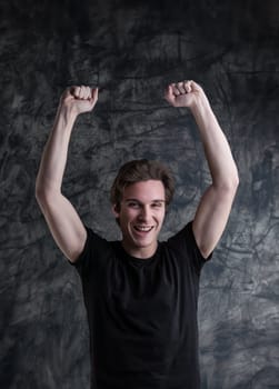 Exuding triumph, a young man in black joyfully raises arms against a grunge board. The epitome of success, victory, and positive outcomes