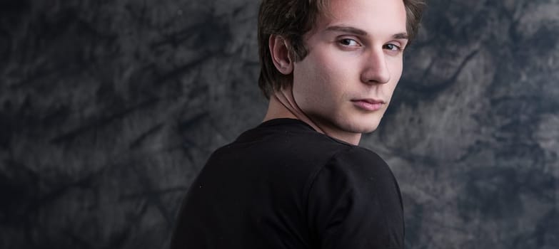 light-brown-haired man, in a black shirt, stands thoughtfully before a grunge blackboard. His introspective gaze offers ample COPYSPACE for content