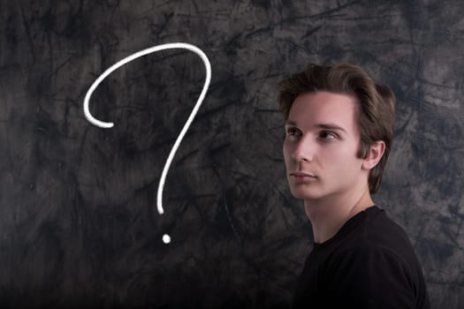 Light-brown-haired man, black shirt, stands before a grunge blackboard. Eyes lifted to a graphic question mark. Symbolizes indecision, choices, stance. Defining moments emerge.