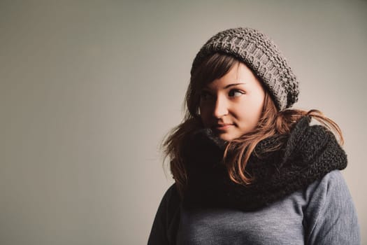 Woman in winter fashion admires the COPYSPACE leftward. Her attire includes woolen gloves, scarf, and cozy sweaters. Brunette locks and lively eyes enhance her look