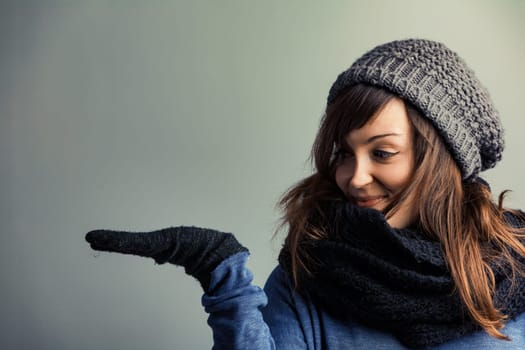 lively young woman in winter attire looks at the expansive COPYSPACE to her left, perfect for your product. She's passionate about this season's fashion. Wool gloves, hat, scarf, and stylish sweaters