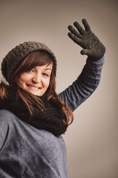 Greeting with a wool-gloved wave, a lively woman expresses her love for winter fashion. She's cozy in her gear, her brown locks and vivacious eyes shining