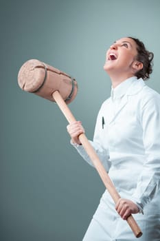With a comedic twist, a scientist holds a hefty wooden mallet, portraying the crude methods in science. Clothed in white, her surroundings in shades of blue-green amplify the humorous yet critical tak