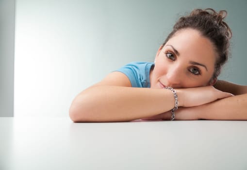 young woman in a blue shirt leans gently on her arms atop an office table, serving as her cushion. She's serenely reflective, contemplating her life's importance and what gives her existence meaning b