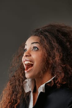 Exuding joy, a stunning black woman with luscious lips gazes upwards, astonished by something positively amazing. Wearing a white shirt, black jacket, and boasting long curly hair, her joy is infectio