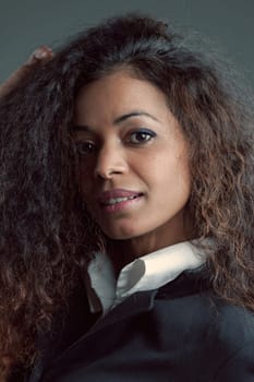 Portrait of Black-skinned Woman and long wavy hair, in elegant white shirt and black jacket. Uncertain expression and poised between a desire for happiness and doubt that it is possible.