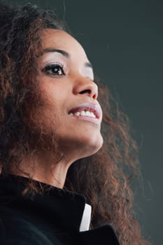 Close-up portrait of the face of a Beautiful Woman with black skin and long wavy hair, dressed in a white shirt and dark jacket. She looks up and is almost in profile, highlighting her stunning little
