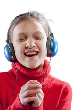 Vibrant young girl in a red sweater, listening to music from the blue headphones she wears on her long brown hair. Dancing and singing, she is enhancing her artistic sensibility. Portrait against a wh