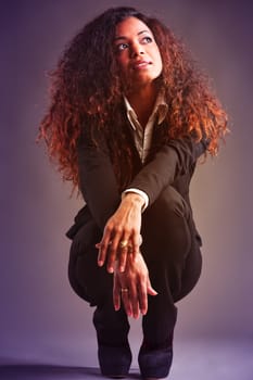 Full-length portrait of Beautiful Woman with black skin and long wavy hair, elegantly dressed, squatting as she looks up amused and thoughtful. 1980s poster atmosphere