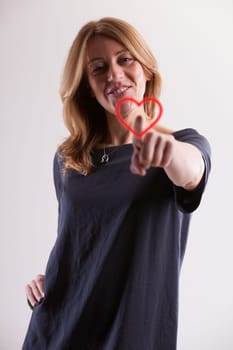 radiant blonde woman around 40, with fair skin, joyfully touches a symbolic heart image. As age demands greater cardiovascular care, love, too, matures and can be cherished more deeply, even on Valent