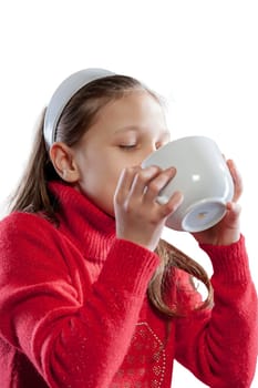 Captured on a white background, a girl in a red sweater with long hair and a white headband, drinks milk voraciously from a large cup for her breakfast or snack