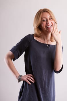 Blonde woman in a gray-blue dress makes a playful gesture as if to hide her laughter. Her unveiled joy champions the freedom of secular civility