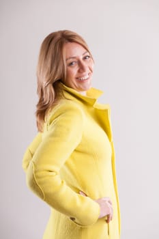 merry adult woman clad in a yellow coat shows off a flirtatious smile. Her portrait stands out against a muted background