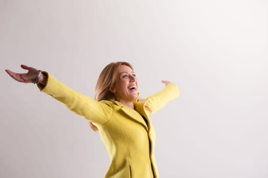 Expressing boundless joy with arms outstretched, a blonde woman savors life's essence. She looks up, recognizing her blessings and showing profound gratitude, smiling past her 40s with self-awareness