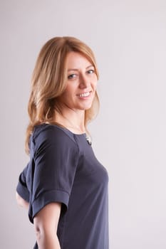confident blonde woman, mid-40s, dons a loose gray-blue dress. Aware of life's hurdles and the importance of autonomy, her professional success stands out, offering inspiration to other women