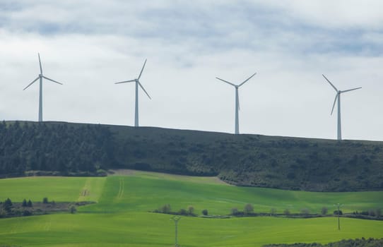 Wind turbines on the top of the hills. Green meadows at the foot of the mountain