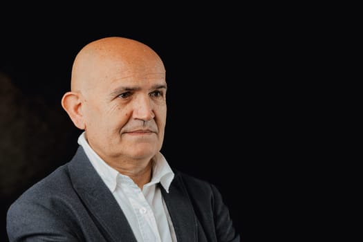 elegant bald elderly man in a blue jacket, set against a blue background beside ample COPYSPACE, gazes aside. He reflects on his past efforts for a better future planet, wondering if his contributions
