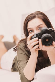 A smiling woman lying on her stomach on the couch at home, with perfectly smooth and hairless legs crossed high behind her bare feet. She's wearing short shorts and a military green shirt and looks th