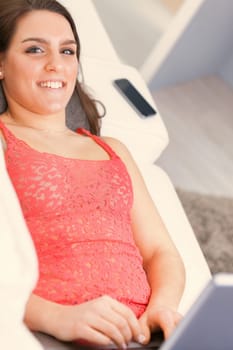 A woman wearing a red lace tank top is busy using her laptop at home. Comfortably on the couch, she can work efficiently without the annoying pressure of the office environment. It's either this or th