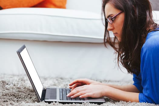 A young woman on the soft and comfortable carpet of her home uses a laptop computer. Is she working, studying, or having fun? Thanks to the wifi and broadband that quickly reach the internet, she does