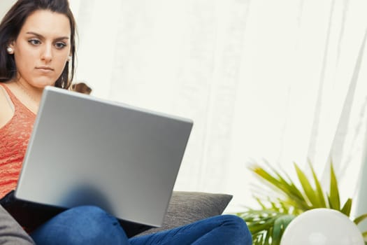 A woman wearing a red lace tank top is busy using her laptop at home. Comfortably on the couch, she can work efficiently without the annoying pressure of the office environment. It's either this or th