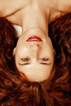 Displayed upside-down, a young woman's vertical portrait mesmerizes. Dominated by her skin and fiery hair, her red lips complement the warmth of her smile. An embodiment of lovable, enviable beauty