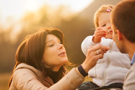 Set against towering mountains, a little girl on a hay bale bursts into laughter, amused by her mother's playful antics with grass. Parents cherish these joyous moments
