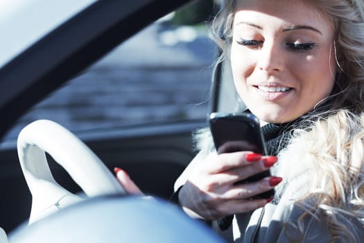 Beautiful young blonde woman with long hair, very outgoing, uses her phone and smartphone while driving a fashionable small car in Europe, about to have fun with friends or as an independent tourist,