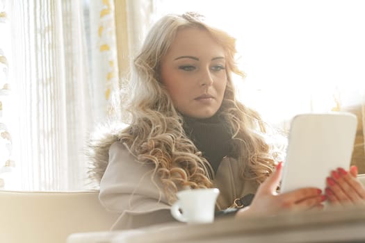 Stunning blonde woman, perfectly dressed, groomed, with makeup and manicure, in a slightly retro elegant European bar, enjoying her espresso while examining her investments and stocks' daily results.