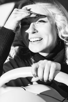 Picture a chic blonde, perfect curls and makeup, navigating a charming European cityscape. Her tiny, fashionable car turns heads as she emphasizes her striking eyes, smiling and shielding from the sun