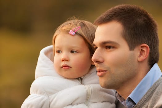 Tender moment captured as father holds young daughter in his arms, their expressions serene against a soft-focus background