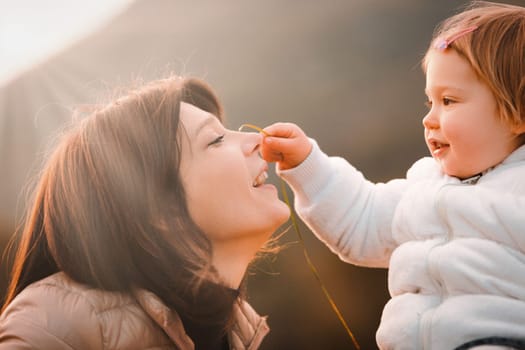 Amidst the cool weather, a mother's love for her young daughter shines brightly. Together outdoors, they find joy in nature's simplicity, under a sky touched by God