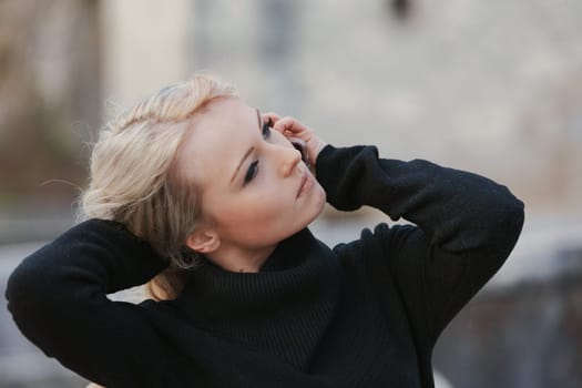 Young woman with long, curly, perfectly permed blonde hair, perfect makeup and manicure, is a tourist in a European city with medieval villages. Using her phone to talk, chat, or access Wi-Fi for hist