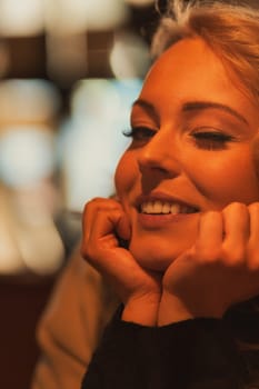 Young woman winks with hands supporting her head from her chin, smiling. She stands inside a warm European, perhaps Italian, club. How nice to travel, she thinks. Maybe I'll meet someone!