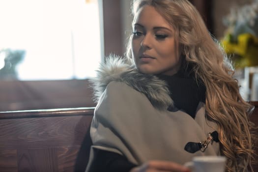 Vibrant traveler relishes espresso in a cozy Euro cafe, basking in sunlit warmth. Winter? No bother! Stylishly snug, savoring her brew, open to connection