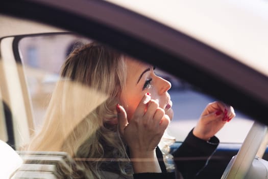 A blonde woman is touching up her makeup or applying it in her car. She is stunning and wants to be perfect for herself and a potential date tonight. She's not a prey but a hunter