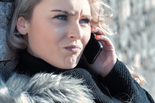 Young woman with long, curly, perfectly permed blonde hair, perfect makeup and manicure, is a tourist in a European city with medieval villages. Using her phone to talk, chat, or access Wi-Fi for hist