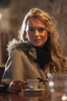 A tourist's chilling at a coffee shop in Europe, enjoying espresso and sun. Winter ain't so bad! Looking great in a fur coat, happy alone or with company