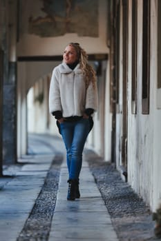 A blonde woman is sightseeing in a historic European city filled with cobblestone streets, archways, marble, and medieval or Gothic elements that have been preserved to appreciate millennial culture a