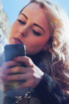 Young woman with long, curly, perfectly permed blonde hair, perfect makeup and manicure, is a tourist in a European city with medieval villages. Using her phone to talk, chat, or access Wi-Fi for hist