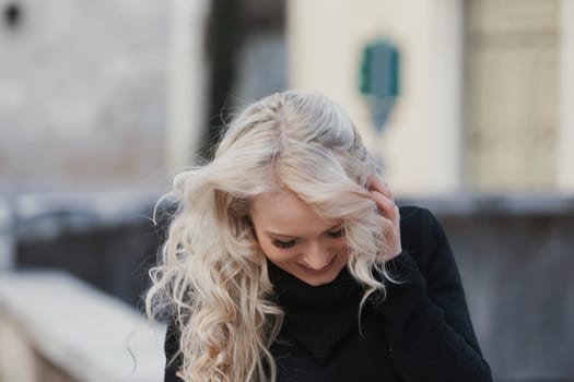 Young woman with long, curly, perfectly permed blonde hair, perfect makeup and manicure, is a tourist in a European city with medieval villages. Using her phone to talk, chat, or access Wi-Fi for hist