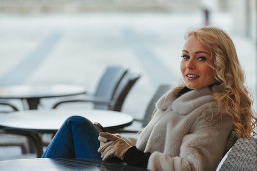 Beautiful young blonde woman sitting at a bar, having fun, laughing at something hilarious on her smartphone or a received message. She's a tourist in a European city, enjoying the fresh air, dressed