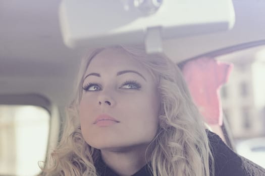 A blonde woman is touching up her makeup or applying it in her car. She is stunning and wants to be perfect for herself and a potential date tonight. She's not a prey but a hunter