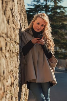 Young woman with long, curly, perfectly permed blonde hair, perfect makeup and manicure, is a tourist in a European city with medieval villages. Using her phone to talk, chat, or access Wi-Fi for hist