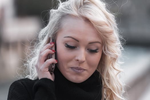 Young woman with long, curly, perfectly permed blonde hair, perfect makeup and manicure, is a tourist in a European city with medieval villages. Using her phone to talk, chat, or access Wi-Fi for hist