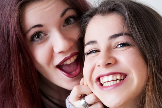 Two young women with meticulous makeup and long hair make goofy faces for selfies. Exuding joy and carefreeness, they playfully experiment with expressions and hairstyles