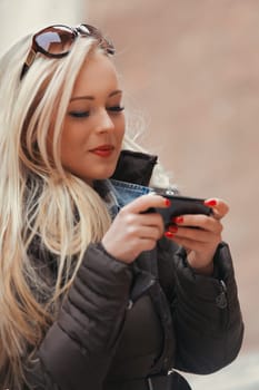 Either as a student or a tourist, a young blonde woman navigates through an ancient European city, using her smartphone for video calls, as a makeshift mirror for makeup, for selfies, and enjoyment