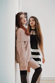 Friends in a photo shoot: one channels chic disarray, the other structured elegance. Thigh-highs, makeup, and poses all work to highlight fleeting youthful charm