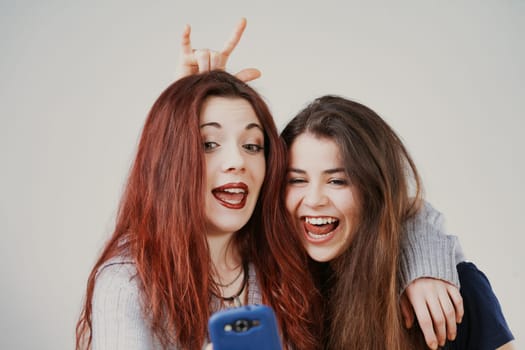 Perfectly groomed yet playful, two young women make amusing faces, possibly for selfies or at a mirror. Their laughter and odd hair antics are infectious